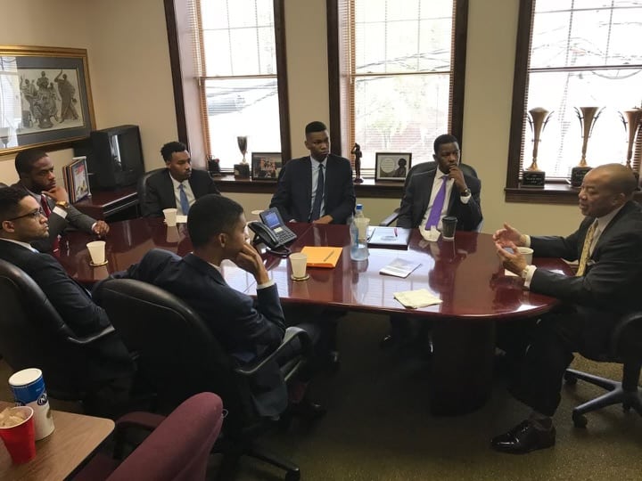 Photo of men in suits seated around a conference table in discussion